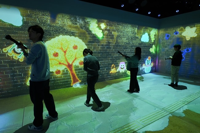 Four people pointing controllers at a wall with visuals projected on it