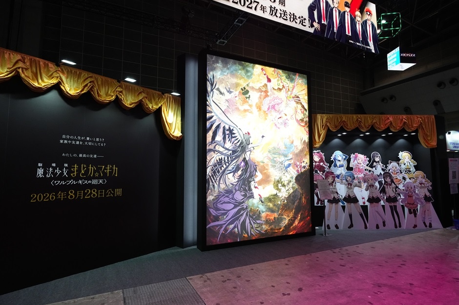 Text on a black wall reads “Puella Magi Madoka Magica the Movie: Walpurgis no Kaiten — In theaters August 28, 2026,” with the film’s key visual displayed beside life-size character standees.