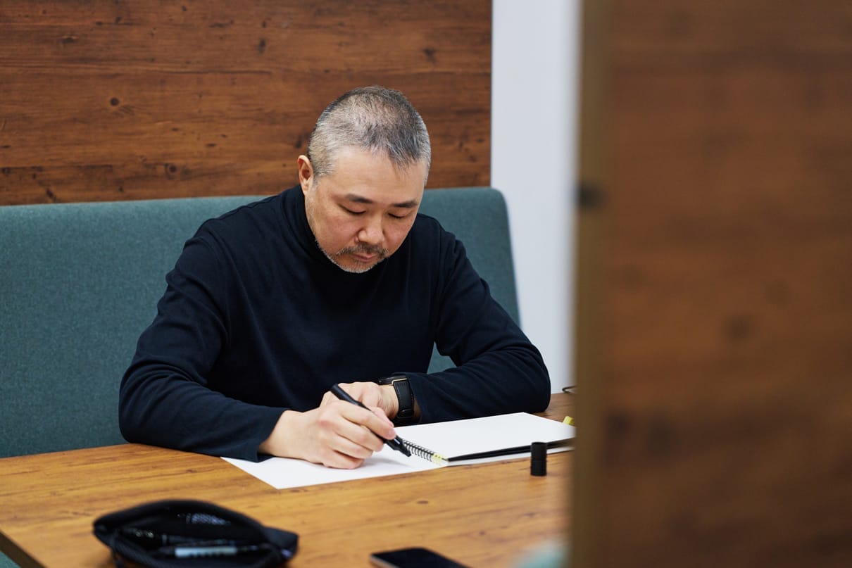 Director Ishihama writes a message in his sketchbook.